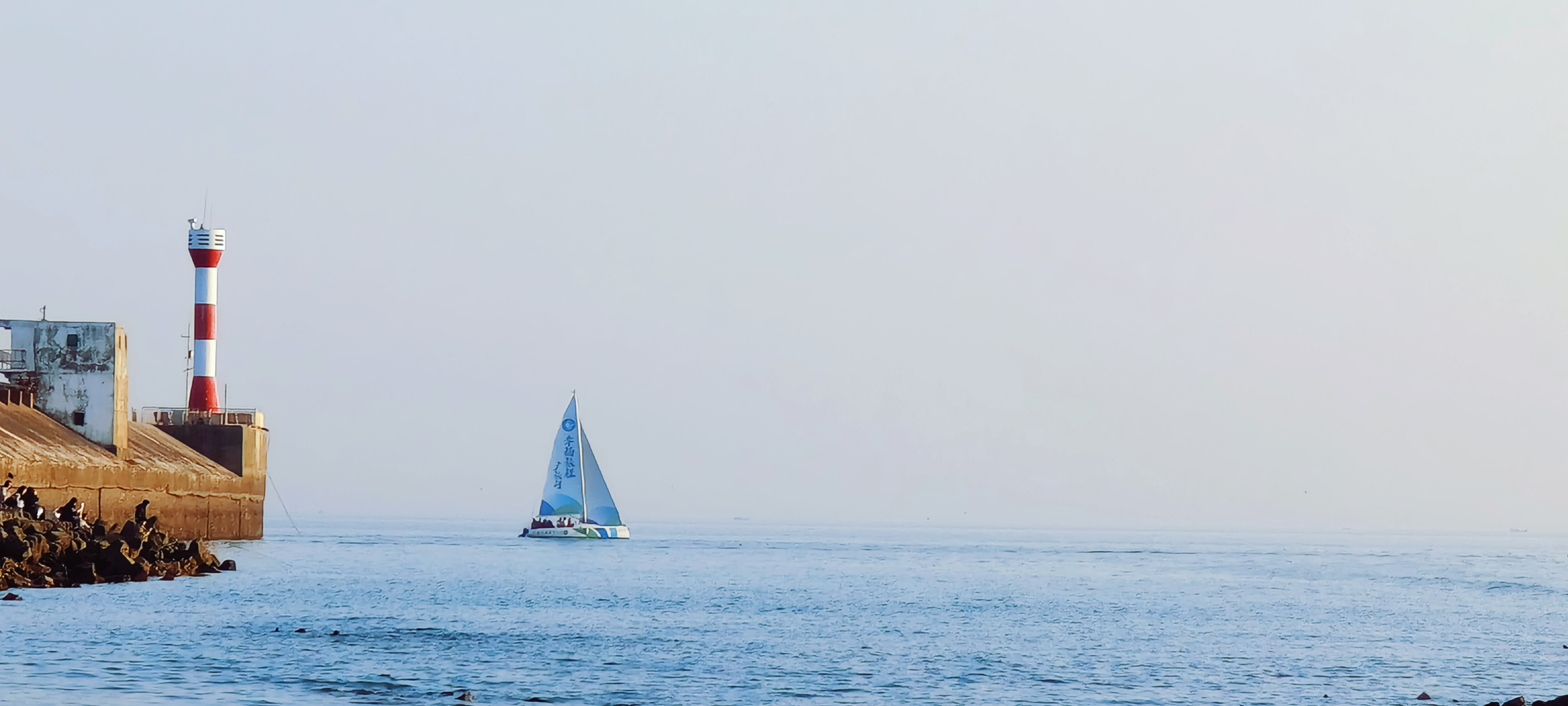 海上灯塔与帆船同框的唯美风景图